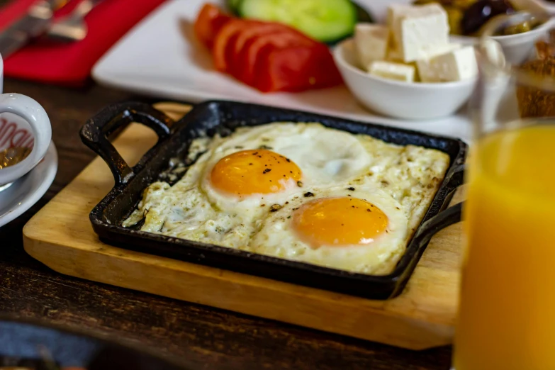 two eggs in a pan on a table with a plate of vegetables and cheese