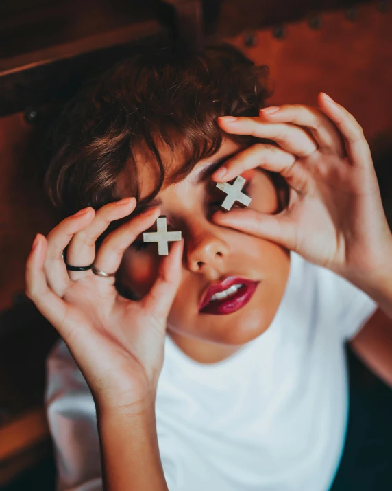 a woman holds up cross and small letter pieces to her eyes