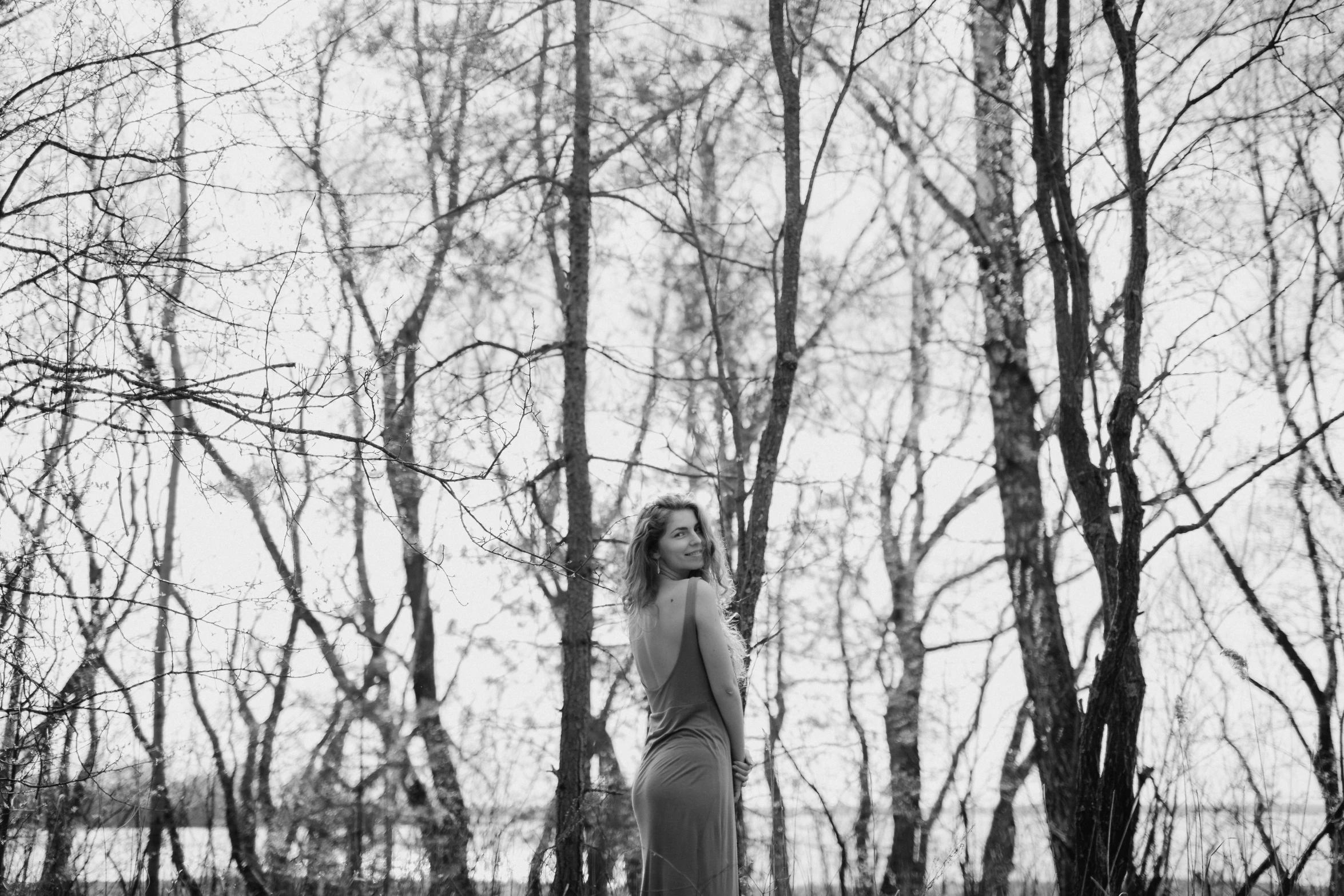 a young woman is standing among the trees in the snow