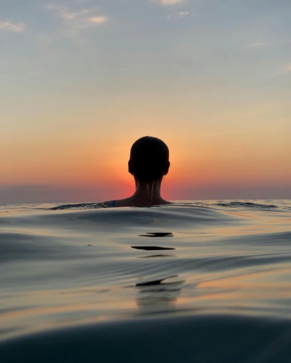 a person in the ocean swimming with a sunset behind them