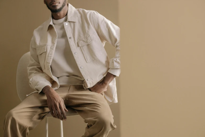 a man is posing for a po, wearing an off white shirt and khaki pants