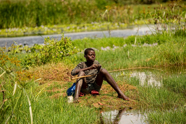 a young african boy sitting in the grass holding a wooden stick