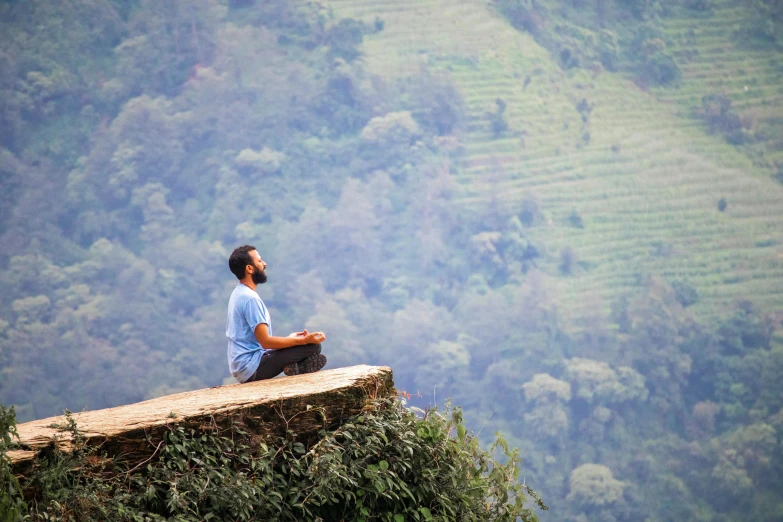 man sitting on cliff above water with view of mountains and valley