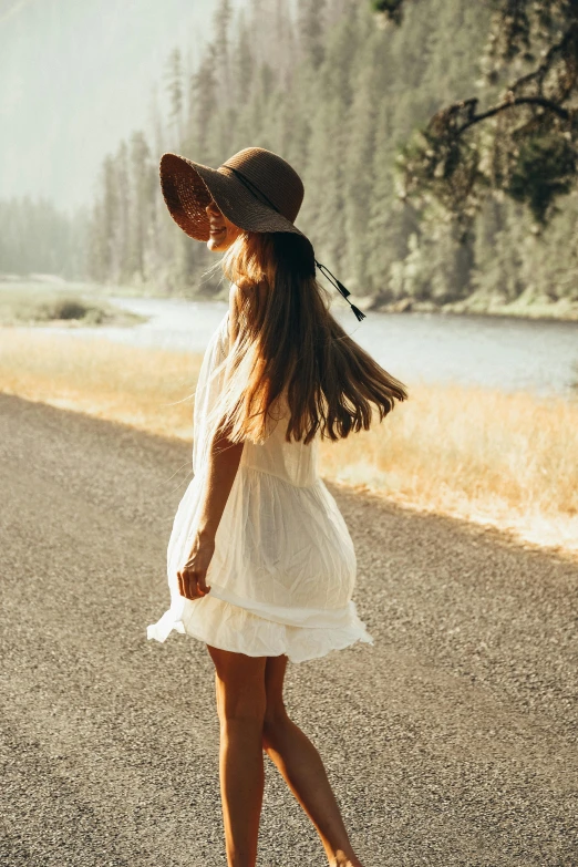 young woman in dress and hat walking on asphalt next to river