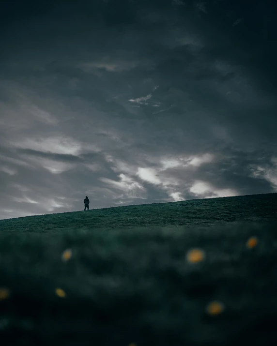 a lone man standing on a hill with dark clouds in the background