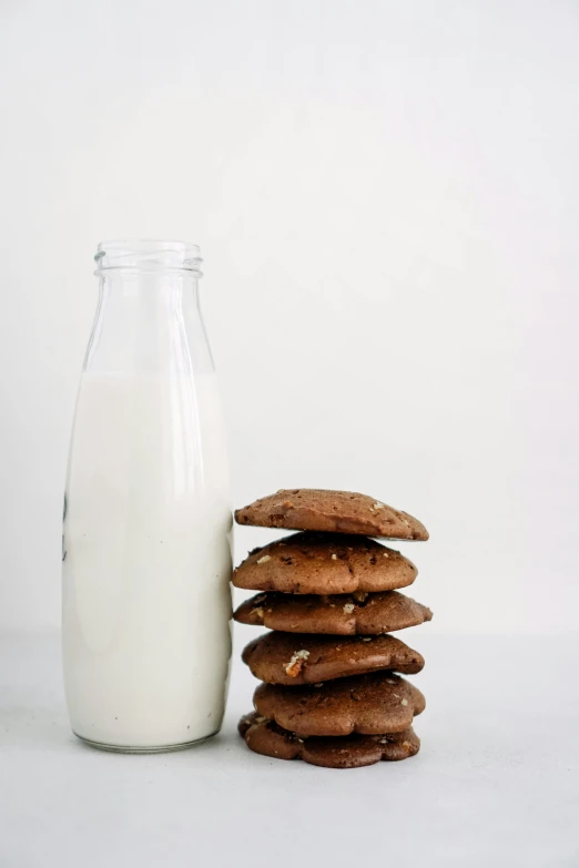 a glass and bottle filled with milk next to cookies