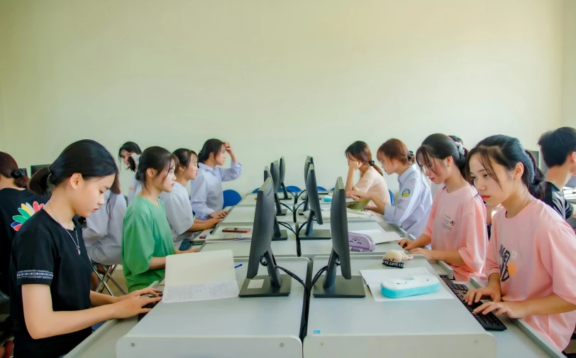 a group of girls sitting at desk working on computers