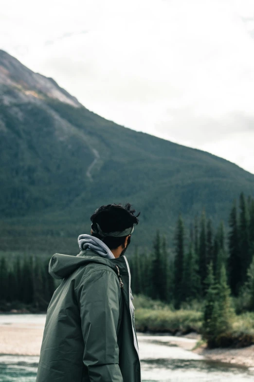 a man with a coat standing next to the edge of a river