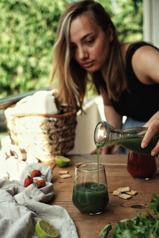 a woman in black shirt pouring a cup with green liquid