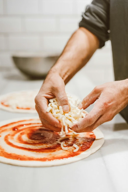 the person is putting shredded cheese on top of a pizza