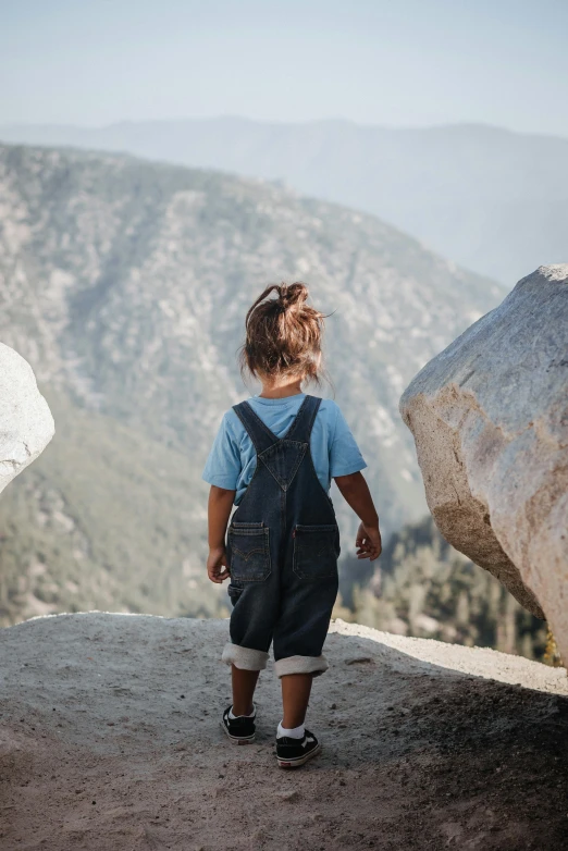 a child looks out at a valley with mountains in the background