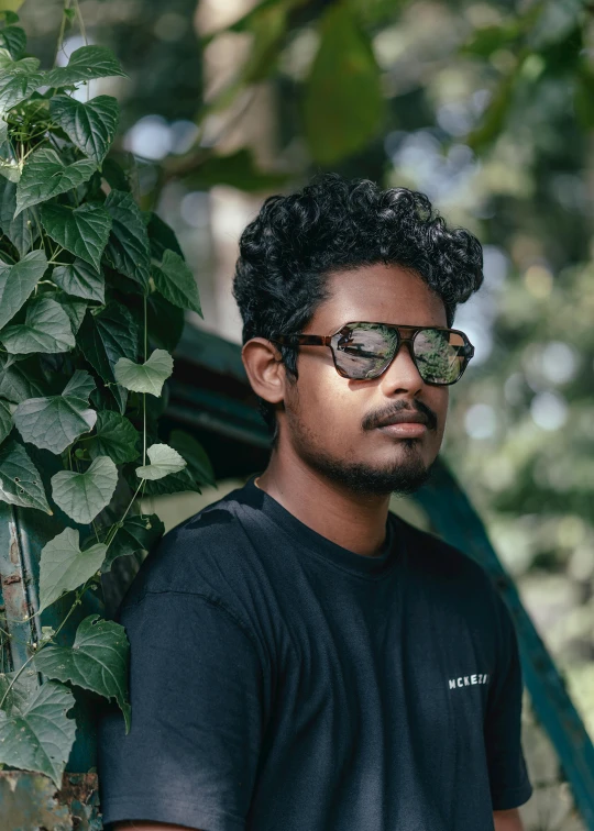 man wearing sunglasses standing next to trees and vines