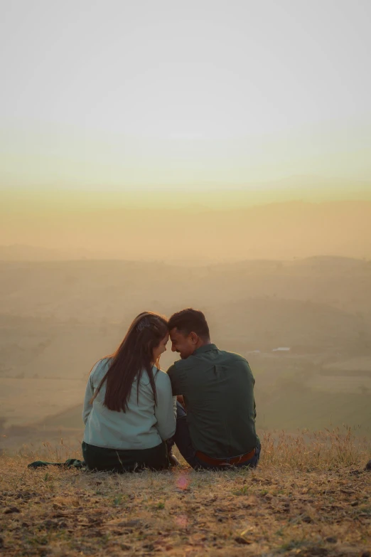 two people sitting on a hill with their arms around each other