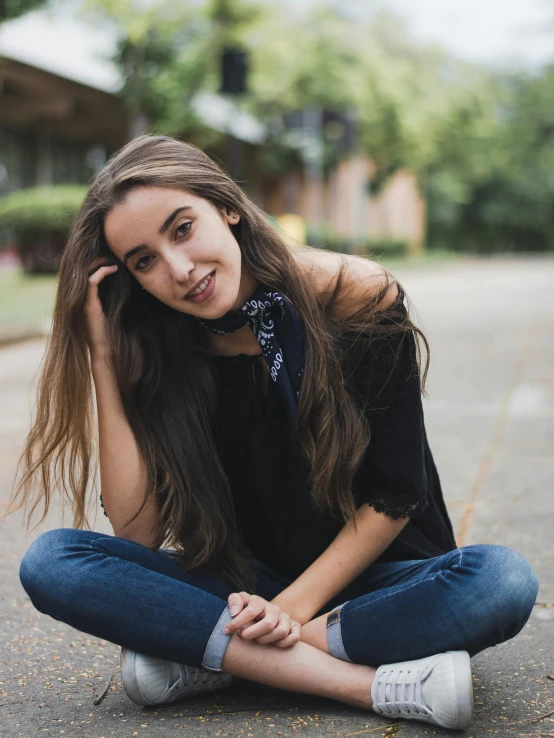 young woman in black top sitting on street in front of trees