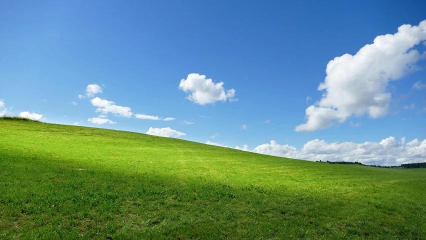 an empty grassy hillside with sky and clouds
