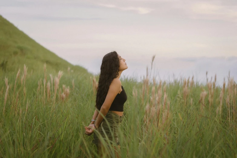 woman looking up in tall grass on the edge of a mountain