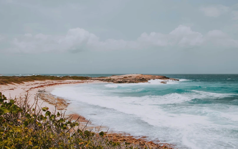 an empty beach with white surf and a small rocky cliff