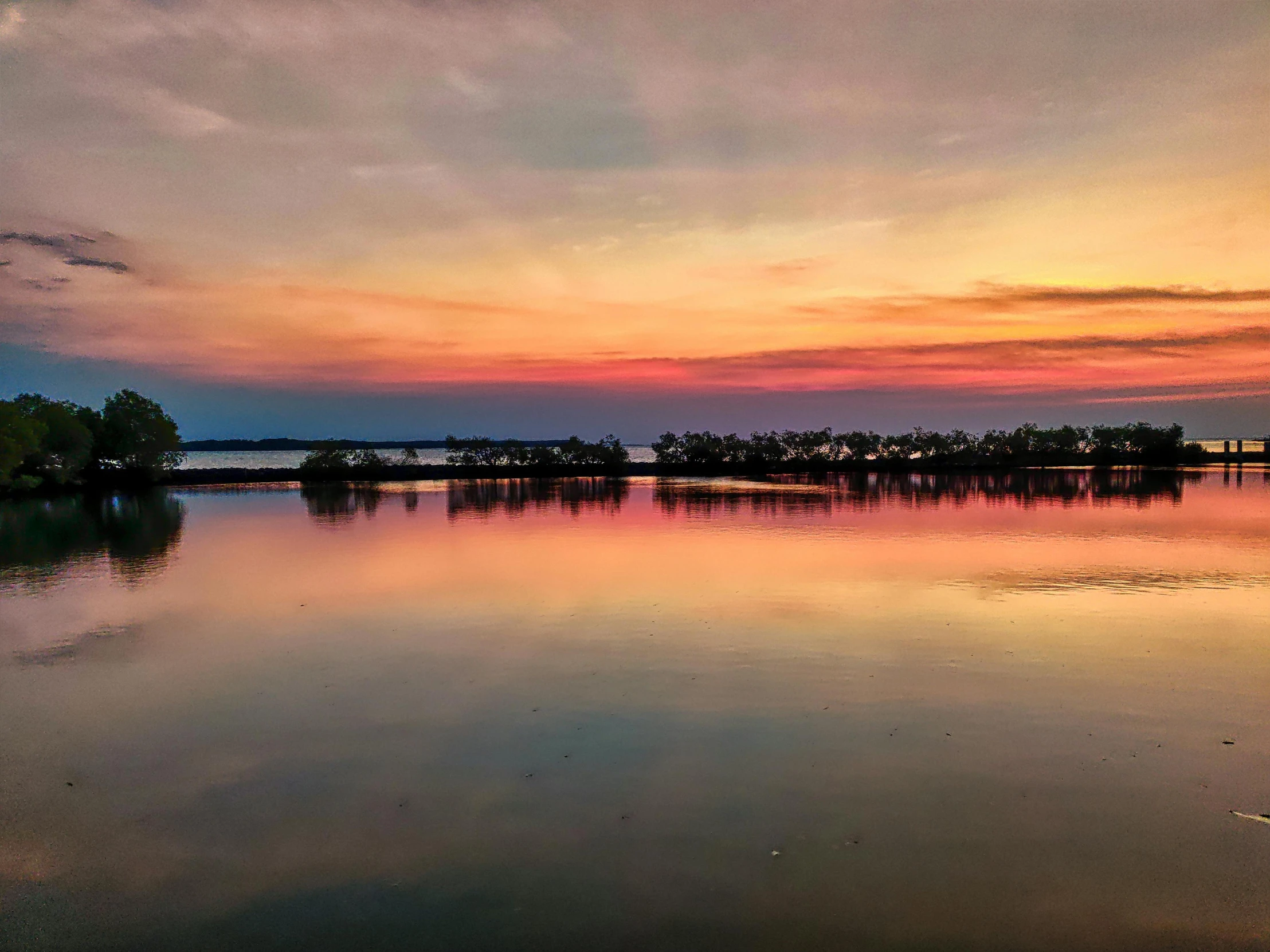 the sun sets on a still lake surrounded by trees