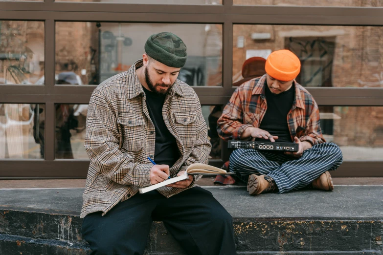 two people on street sitting by side of wall, one reading a book and the other holding an orange frisbee