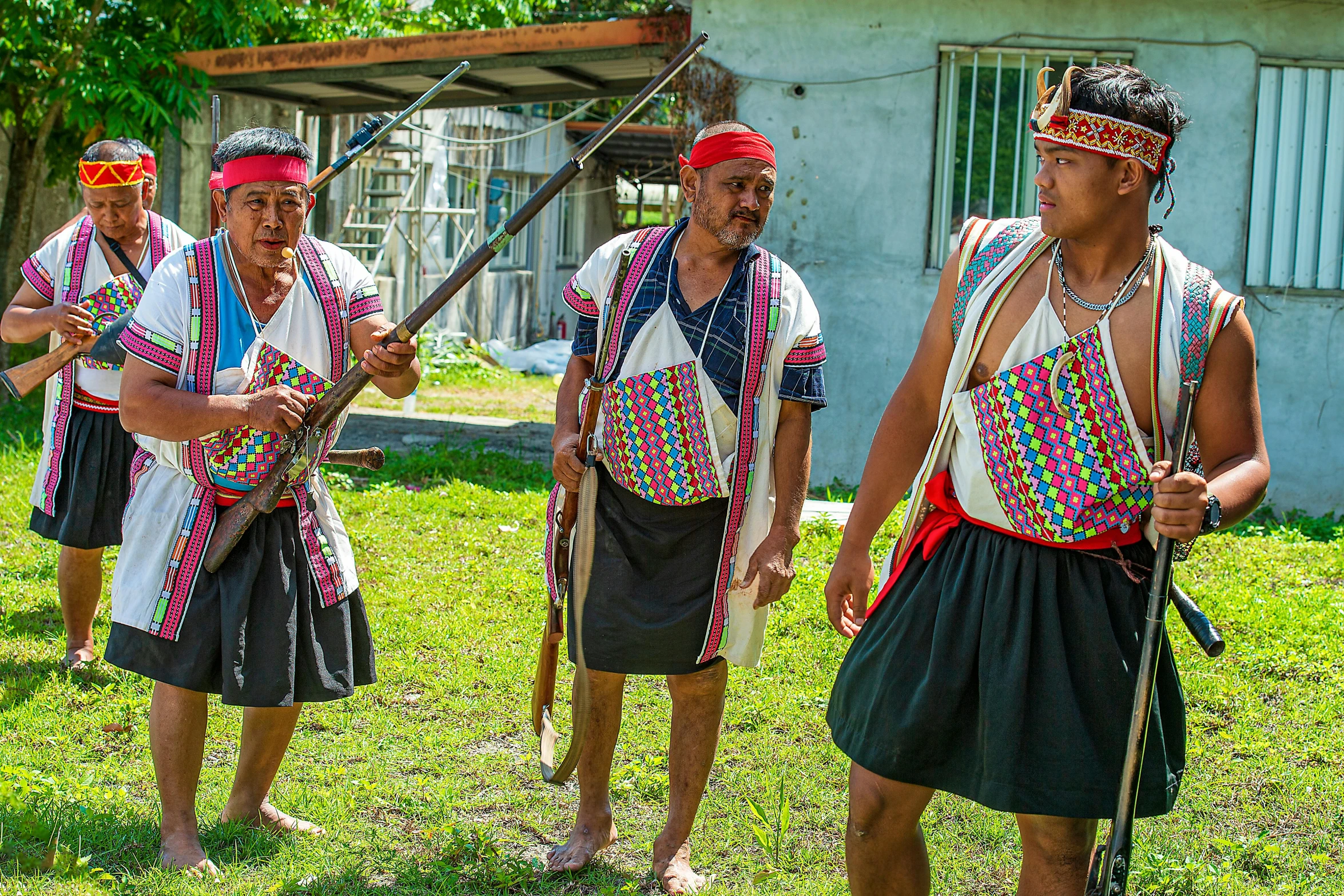 three men wearing traditional garb in front of a house