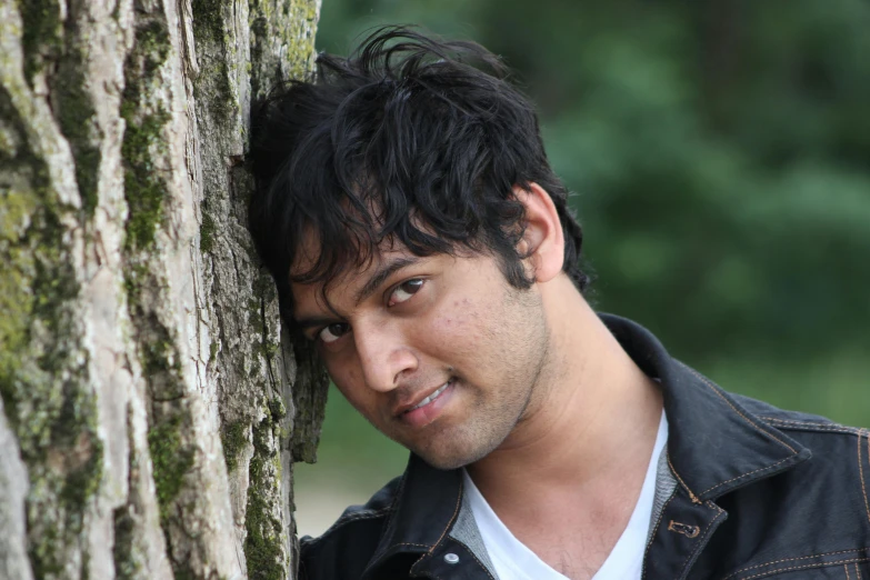 a man with dark hair leaning against a tree