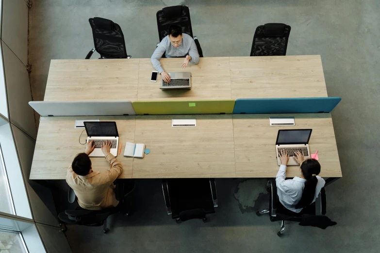 three people are seated at desks with laptop computers