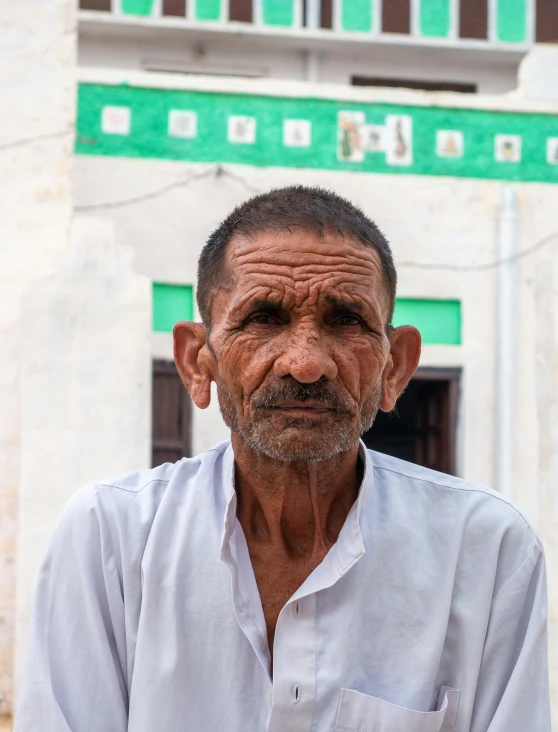 a man with a white shirt and beard standing in front of a building