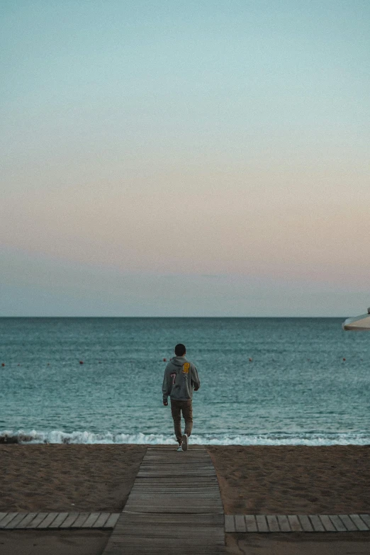 a man walking on the boardwalk next to the ocean