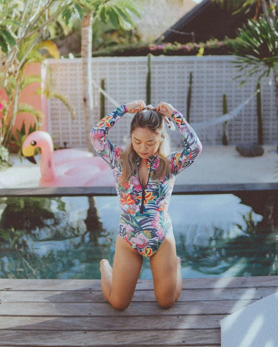 a beautiful young woman sitting on a wooden deck next to a pool