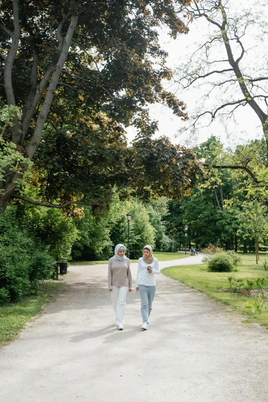 two ladies walking down a dirt road in the middle of a forest