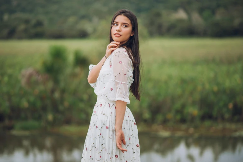 a woman wearing a dress stands by a lake