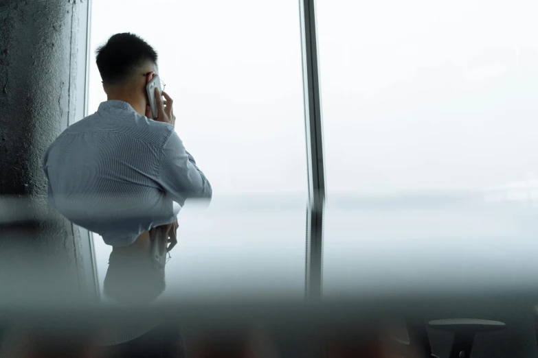 a man sits in front of an open window while on his cell phone