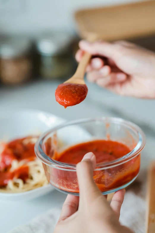 someone spooning a spoonful of marinara sauce out of a glass bowl