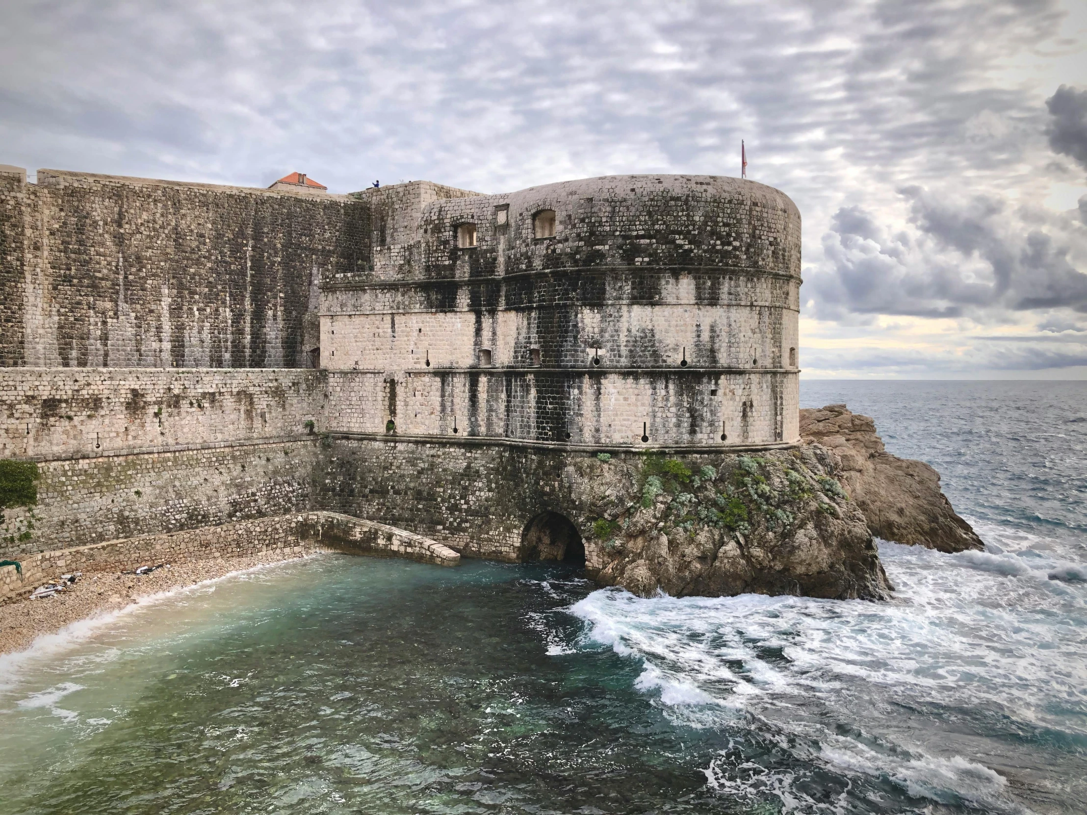 a stone wall by the ocean with water and clouds