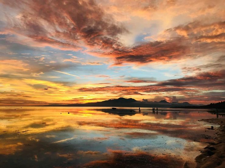 a beautiful sunset reflecting off the ocean and people walking along the shore