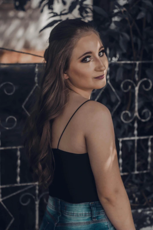 a girl with long hair in a tank top standing by the iron fence