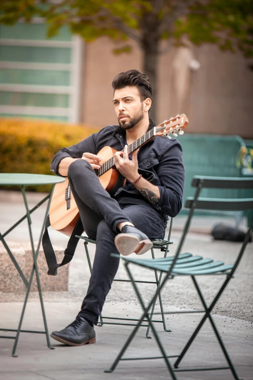 man in black jacket sitting on chair with guitar