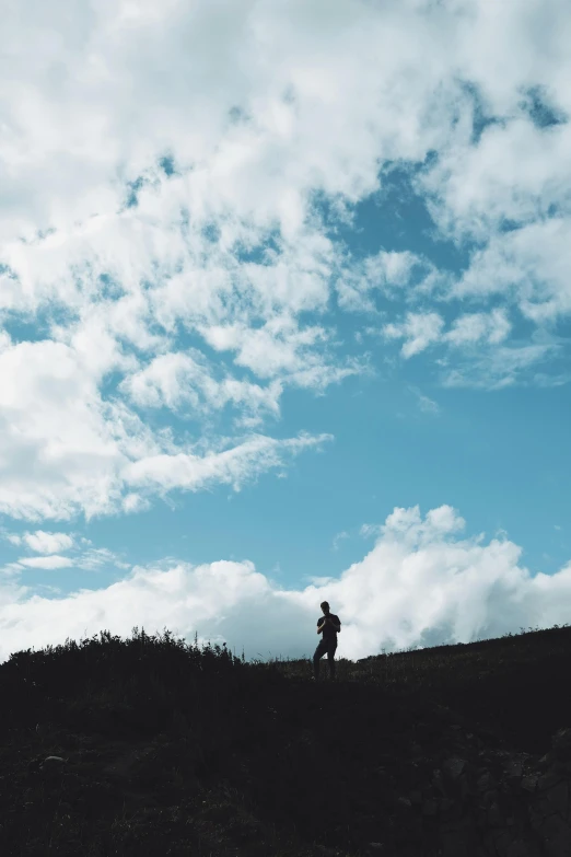 the man is hiking up a hill on a cloudy day