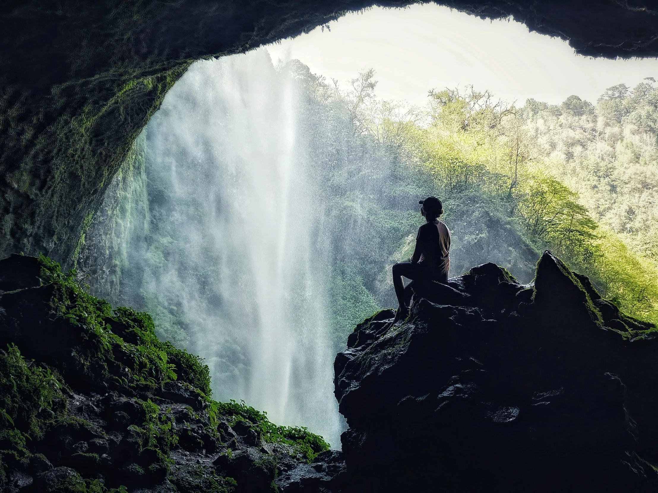 a person on a rock and a view of the waterfall