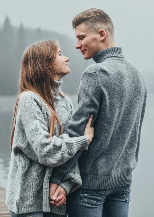 a smiling young man and woman leaning on each other near the water