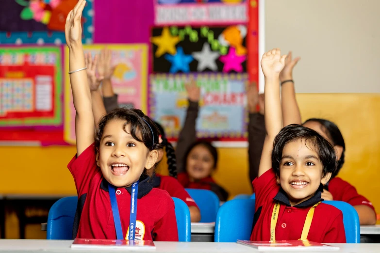 a boy and girl at their desks raising their hands