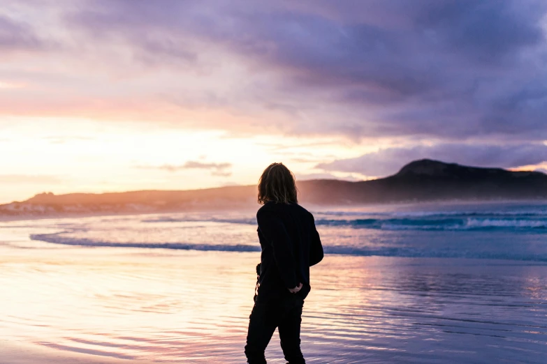 a person with long hair standing on the beach