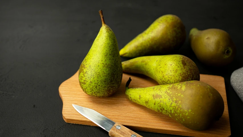 four pears sitting on a  board with a knife