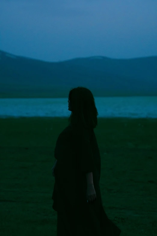 a woman standing on a grass field next to a body of water