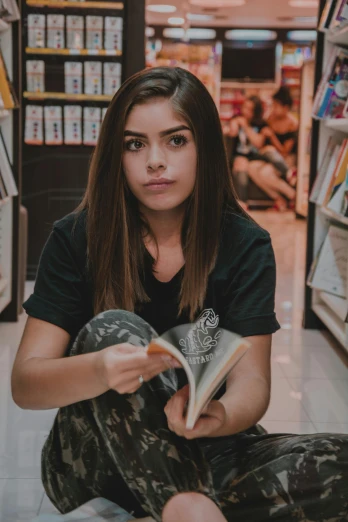 a girl in camouflage print pants sitting on the ground while reading a book