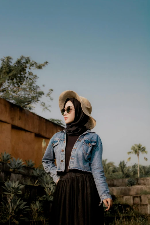 a woman wearing sunglasses and a denim jacket standing in a field