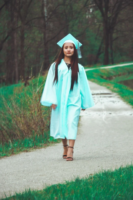 a girl in a graduation gown and cap walks down a path
