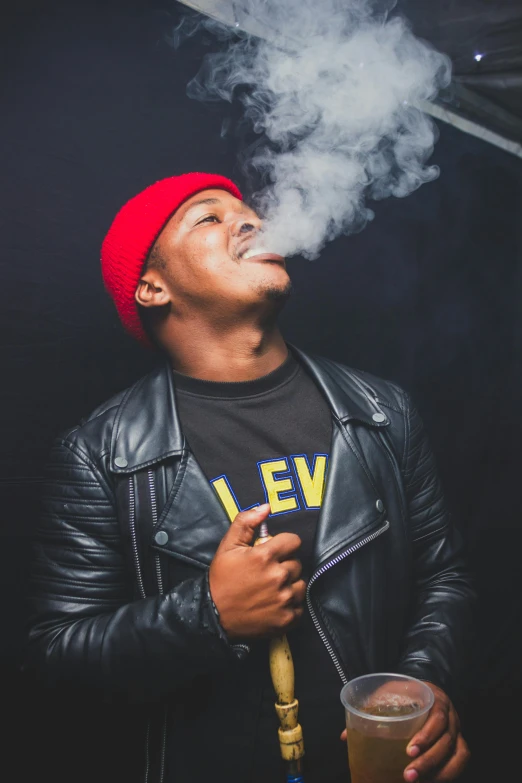 man in black jacket smoking cigarette next to glass