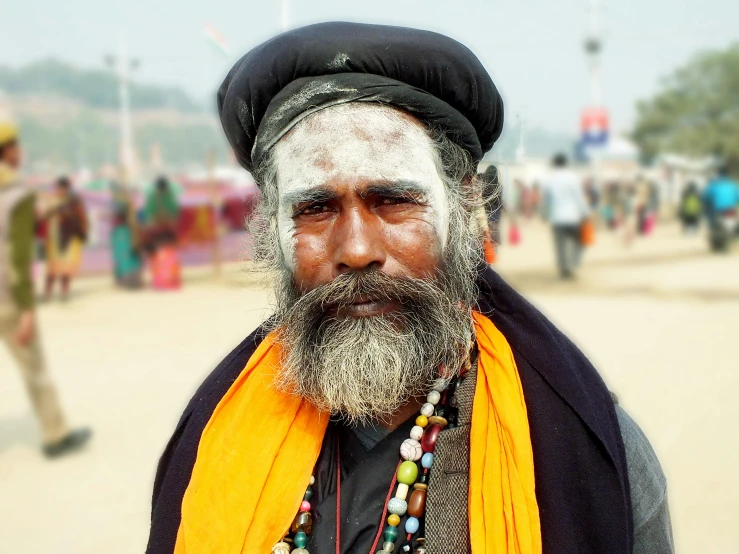 a man with white and orange paint on his face, wearing a black turban