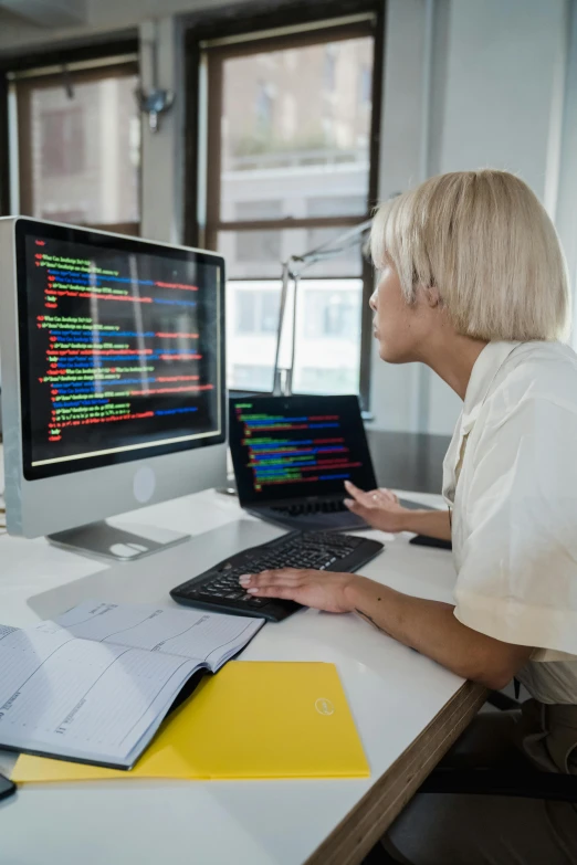 a woman on a laptop and a monitor sitting beside a keyboard